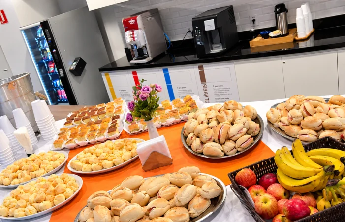 Mesa de coffee break da Mamanduca para evento corporativo em Barueri, com mini sanduíches, pães de queijo, salgados, frutas frescas e bebidas.