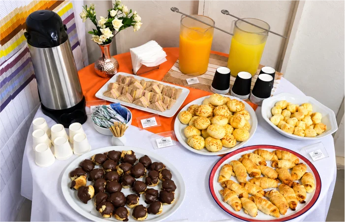 Mesa de buffet para evento corporativo preparada pela Mamanduca, com mini sanduíches, pães de queijo, salgados, doces, café e sucos.